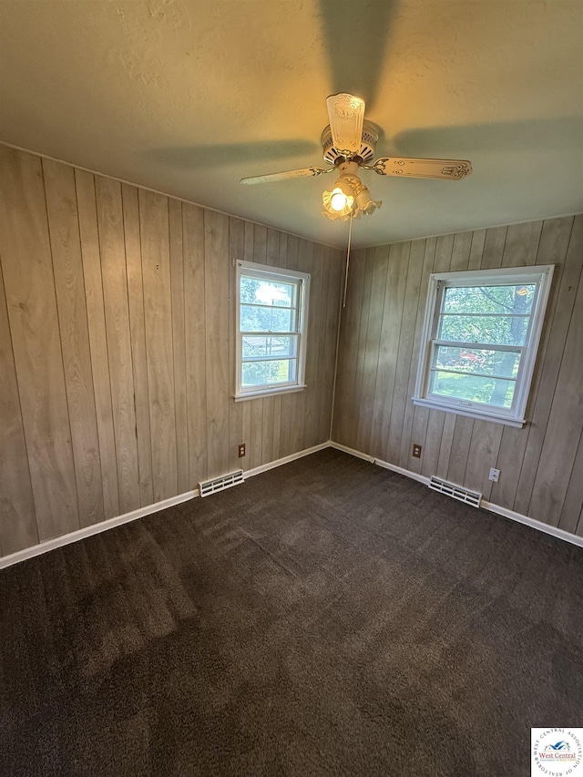 7801 Ozark Rd, Kansas City, MO 64129 - spare room with a ceiling fan, wood walls, dark carpet, and a textured ceiling