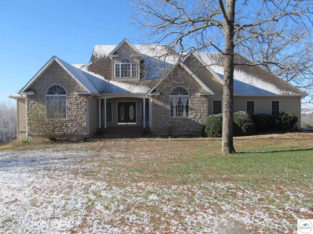 view of front of home with roof with shingles, a front yard, and stone siding