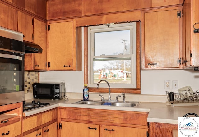 kitchen featuring a sink, light countertops, under cabinet range hood, black appliances, and backsplash