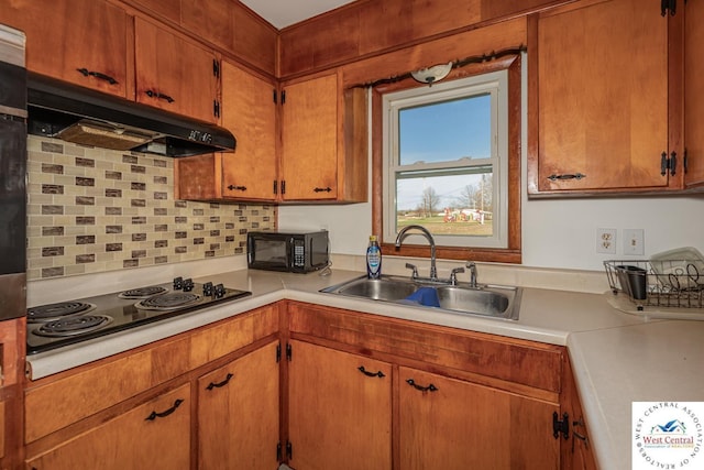 kitchen with a sink, under cabinet range hood, black appliances, backsplash, and light countertops