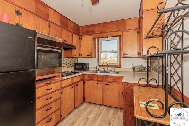 kitchen with a sink, decorative backsplash, light wood-type flooring, black appliances, and light countertops