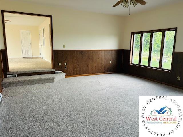 45869 E Hwy, Milan, MO 63556 - spare room featuring a wainscoted wall, a ceiling fan, carpet flooring, and wood walls