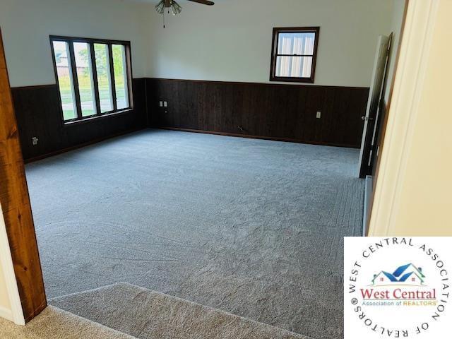 45869 E Hwy, Milan, MO 63556 - carpeted empty room with a wainscoted wall, a ceiling fan, and wood walls