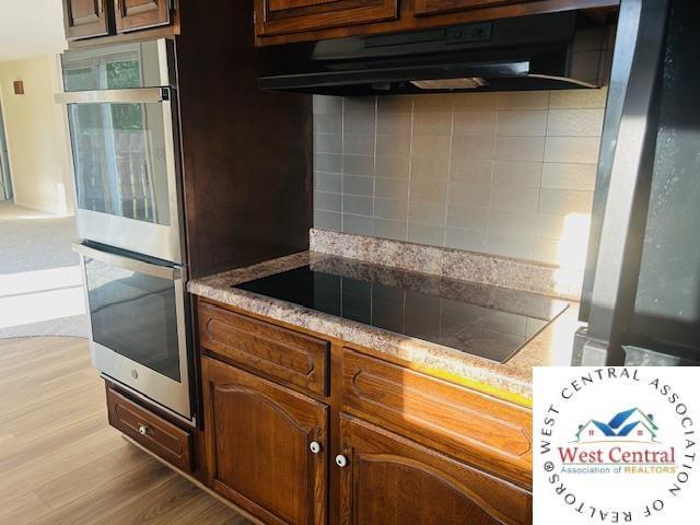 45869 E Hwy, Milan, MO 63556 - kitchen featuring double oven, under cabinet range hood, light wood-style flooring, backsplash, and black electric stovetop