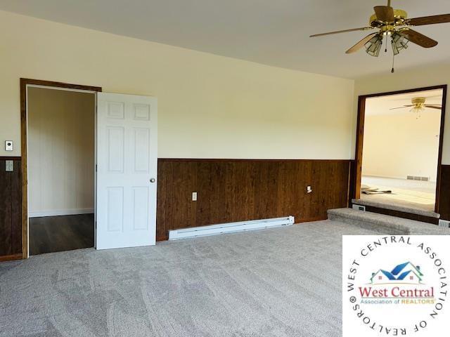 45869 E Hwy, Milan, MO 63556 - unfurnished room with a ceiling fan, wainscoting, carpet floors, a baseboard radiator, and wooden walls
