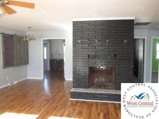 unfurnished living room with wood finished floors, ceiling fan with notable chandelier, a fireplace, baseboards, and visible vents