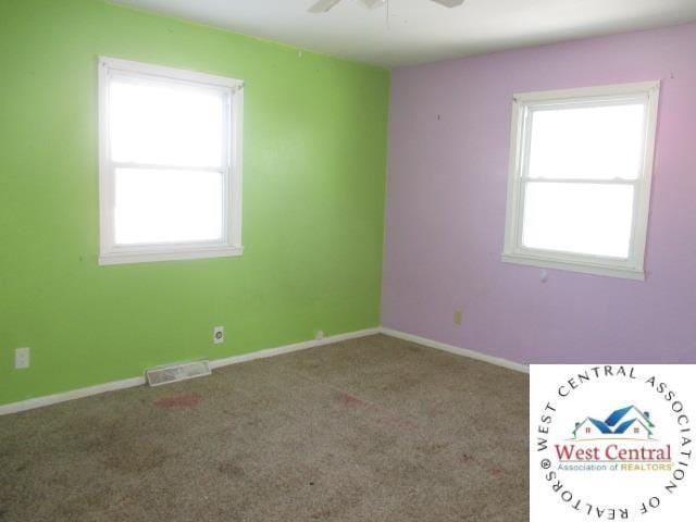 carpeted empty room with visible vents, a ceiling fan, and baseboards