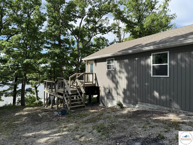 view of home's exterior with a shingled roof, a wooden deck, and stairway