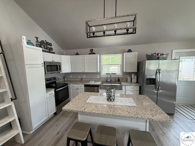 kitchen featuring stainless steel appliances, a sink, a breakfast bar area, white cabinetry, and light wood-style floors