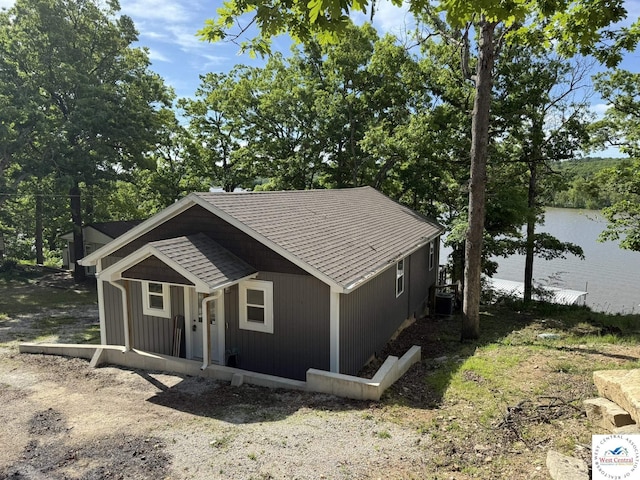 single story home with central air condition unit, a shingled roof, and a water view