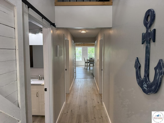 hall featuring a sink, baseboards, and light wood-style flooring