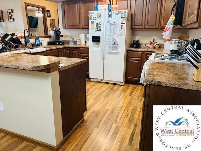 913 S Main St, Milan, MO 63556 - kitchen featuring white refrigerator with ice dispenser, black microwave, a sink, light wood-type flooring, and a peninsula