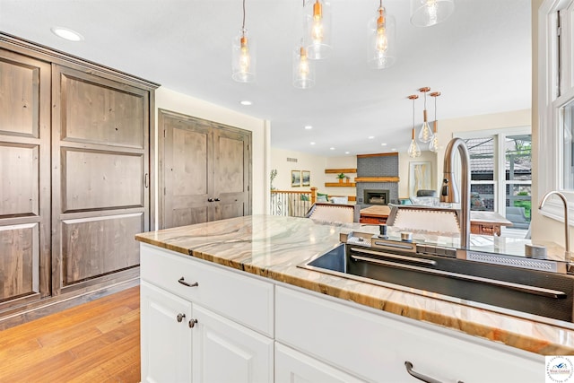 1715 Sycamore Dr, Sedalia, MO 65301 - kitchen featuring a sink, a fireplace, light wood-type flooring, light stone counters, and hanging light fixtures