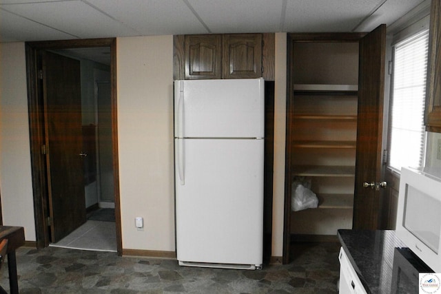kitchen with baseboards, a drop ceiling, and freestanding refrigerator