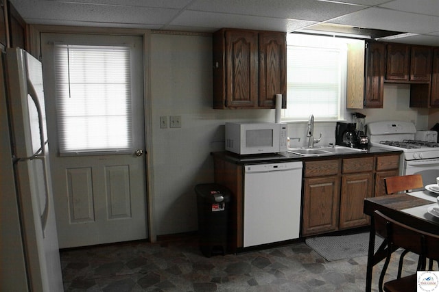 kitchen featuring white appliances, stone finish floor, dark countertops, a sink, and a paneled ceiling
