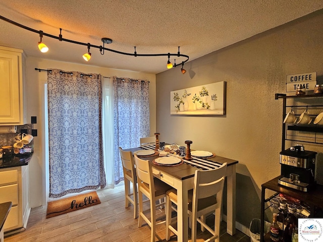 dining space with a textured ceiling, light wood-style floors, and a textured wall
