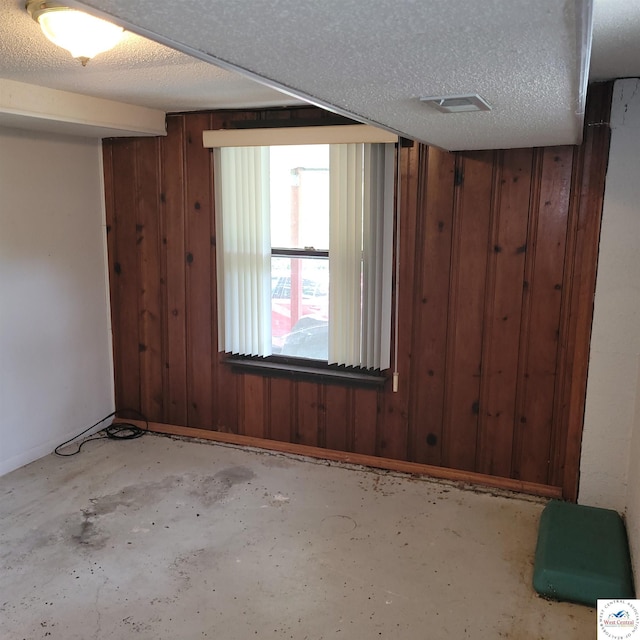 empty room featuring wooden walls, unfinished concrete floors, and baseboards