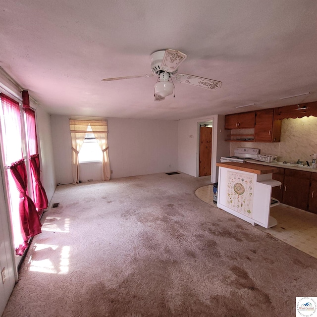 unfurnished living room featuring light carpet, a ceiling fan, and a sink