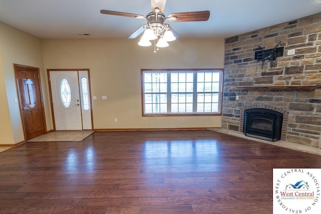 unfurnished living room with wood finished floors, a ceiling fan, a stone fireplace, and baseboards
