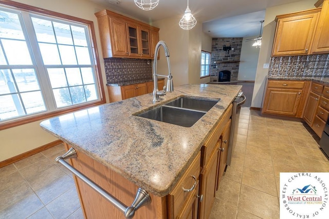 kitchen featuring tasteful backsplash, an island with sink, brown cabinetry, and a sink
