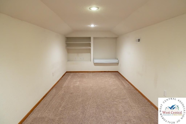 carpeted empty room featuring visible vents, lofted ceiling, and baseboards