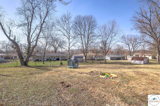view of yard featuring a trampoline, an outbuilding, a residential view, a storage unit, and fence