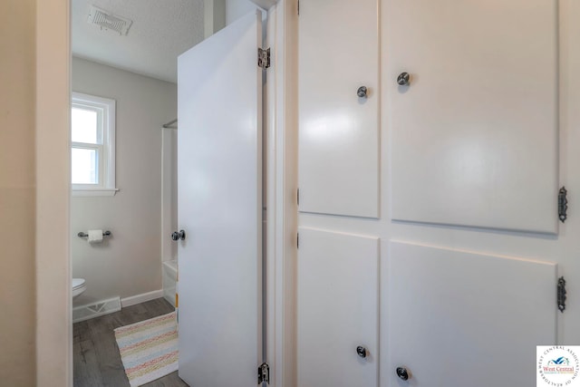 bathroom with bathing tub / shower combination, toilet, visible vents, baseboards, and wood finished floors