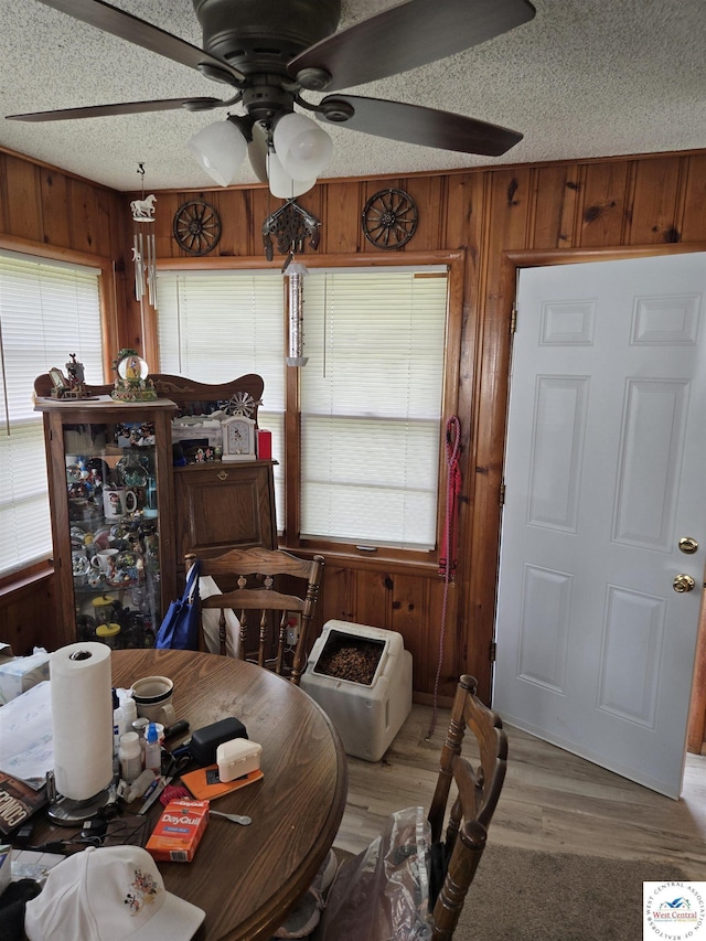 dining space featuring wood walls, ceiling fan, wood finished floors, and a healthy amount of sunlight