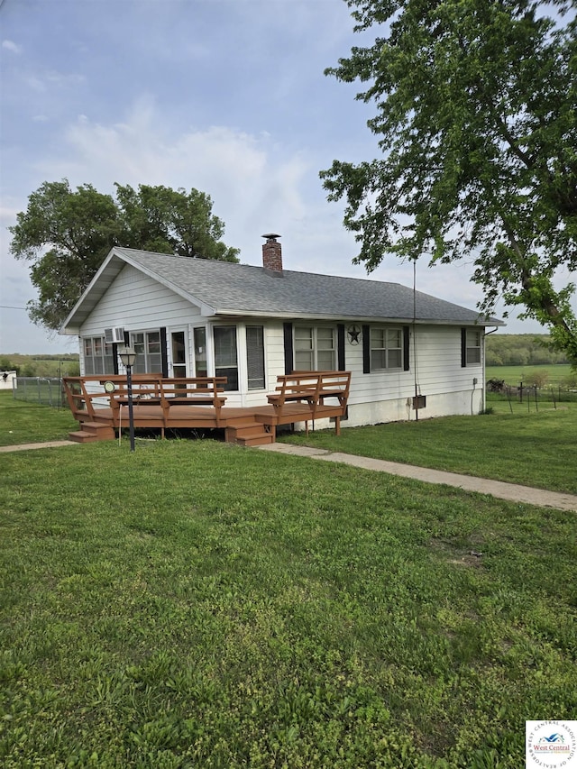 rear view of house with fence, a wooden deck, a chimney, a shingled roof, and a yard