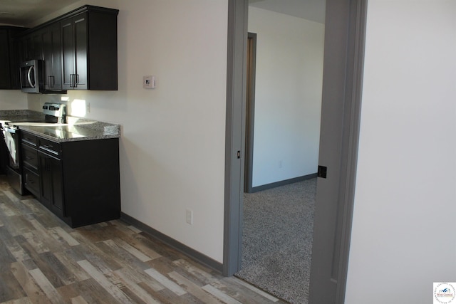 kitchen featuring stainless steel microwave, baseboards, light wood finished floors, range with electric stovetop, and dark cabinetry