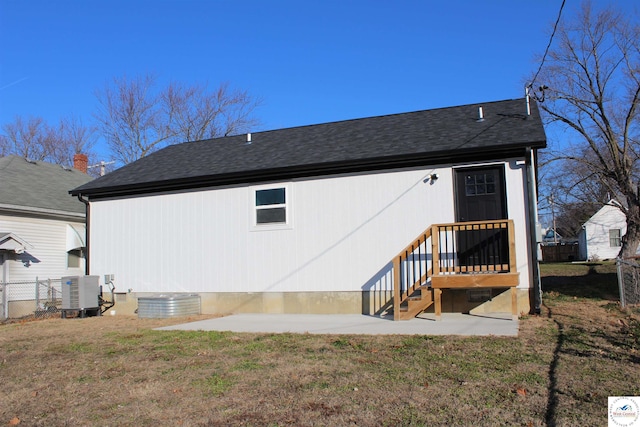 back of property featuring a yard, central AC unit, a shingled roof, and fence