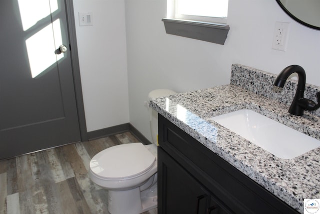 half bathroom featuring toilet, wood finished floors, and vanity
