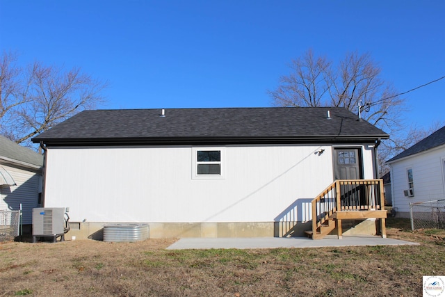 back of property with cooling unit, a yard, a shingled roof, and fence