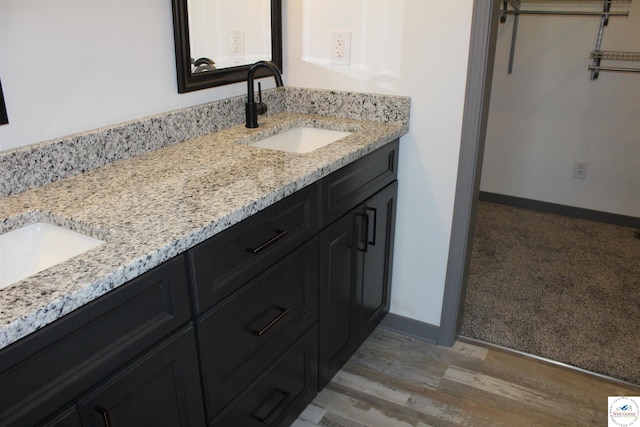 full bath with double vanity, a sink, wood finished floors, and baseboards