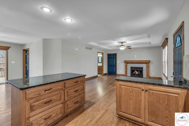 21439 Lost Rd, Warsaw, MO 65355 - kitchen featuring a raised ceiling, ceiling fan, a fireplace, and light wood-style flooring