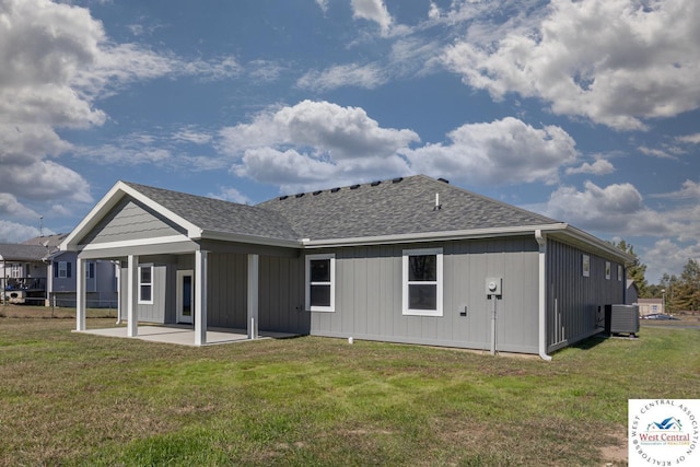 rear view of house with a lawn, roof with shingles, board and batten siding, and a patio area