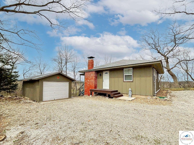 view of front of property with an outbuilding, a detached garage, board and batten siding, a chimney, and gravel driveway