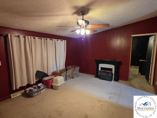 unfurnished living room with a ceiling fan, a textured ceiling, carpet, and a fireplace