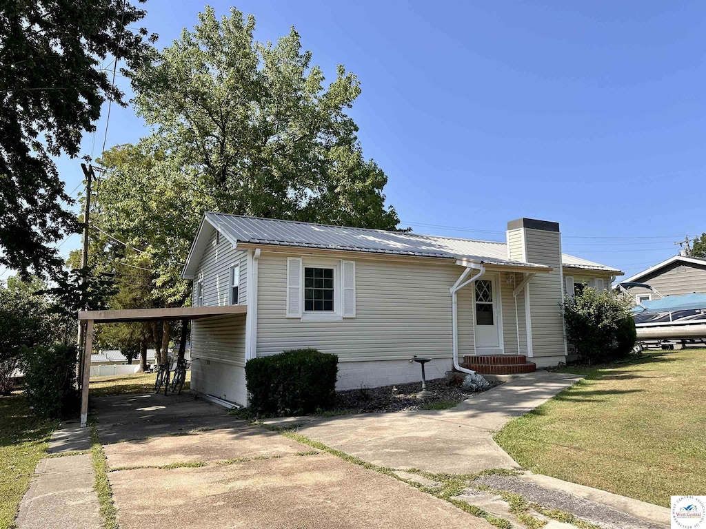 view of front of property with driveway, a carport, a chimney, metal roof, and a front lawn