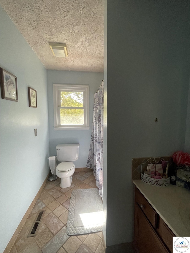 bathroom with toilet, vanity, a textured ceiling, visible vents, and baseboards