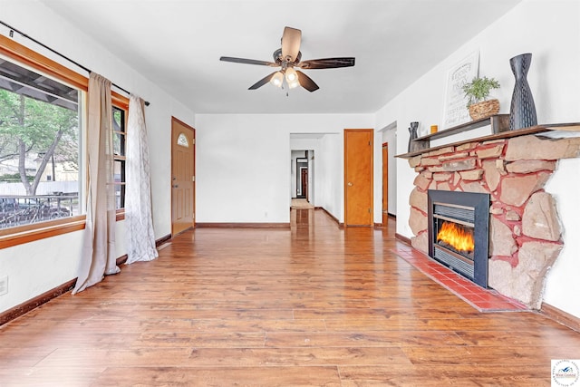 unfurnished living room featuring baseboards, ceiling fan, a fireplace, and light wood-style flooring