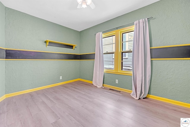 unfurnished room with a textured wall, a ceiling fan, baseboards, wood finished floors, and visible vents