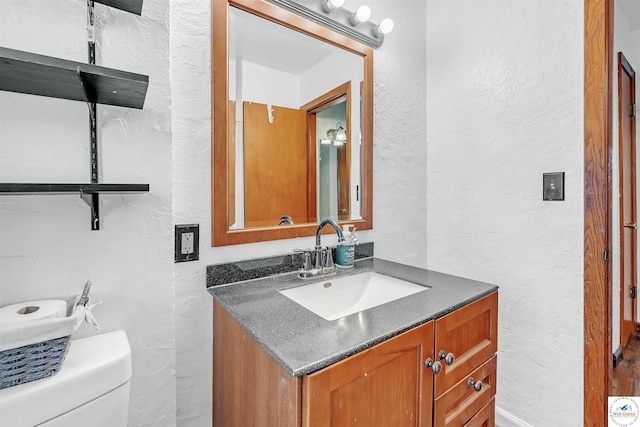 bathroom with vanity, a textured wall, and toilet