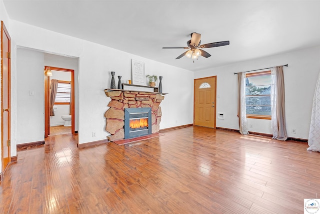 unfurnished living room featuring wood finished floors, ceiling fan, a stone fireplace, and a wealth of natural light