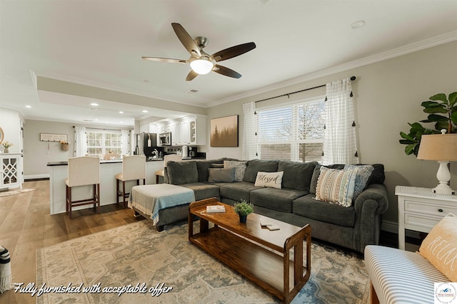 living room with a healthy amount of sunlight, wood finished floors, a ceiling fan, and crown molding