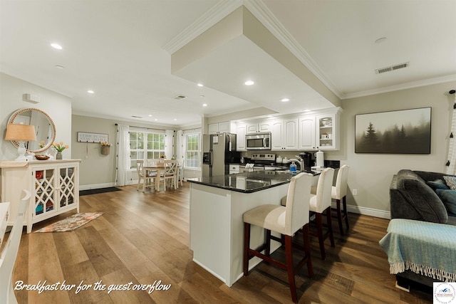 kitchen featuring stainless steel appliances, white cabinets, ornamental molding, a kitchen bar, and visible vents