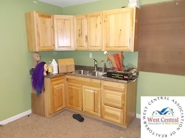 kitchen featuring a sink, light colored carpet, light brown cabinets, baseboards, and dark countertops