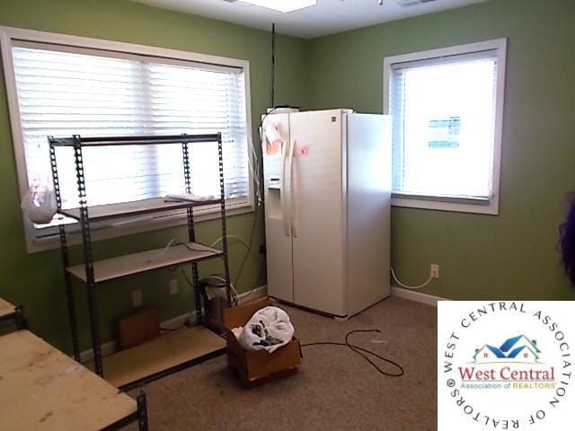 carpeted bedroom with baseboards, white fridge with ice dispenser, and multiple windows