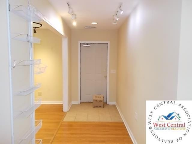 hallway with rail lighting, light wood-style floors, visible vents, and baseboards