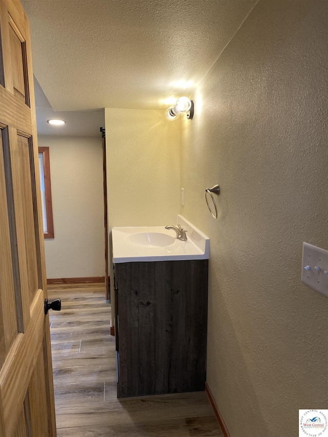 bathroom featuring baseboards, wood finished floors, a textured ceiling, and vanity